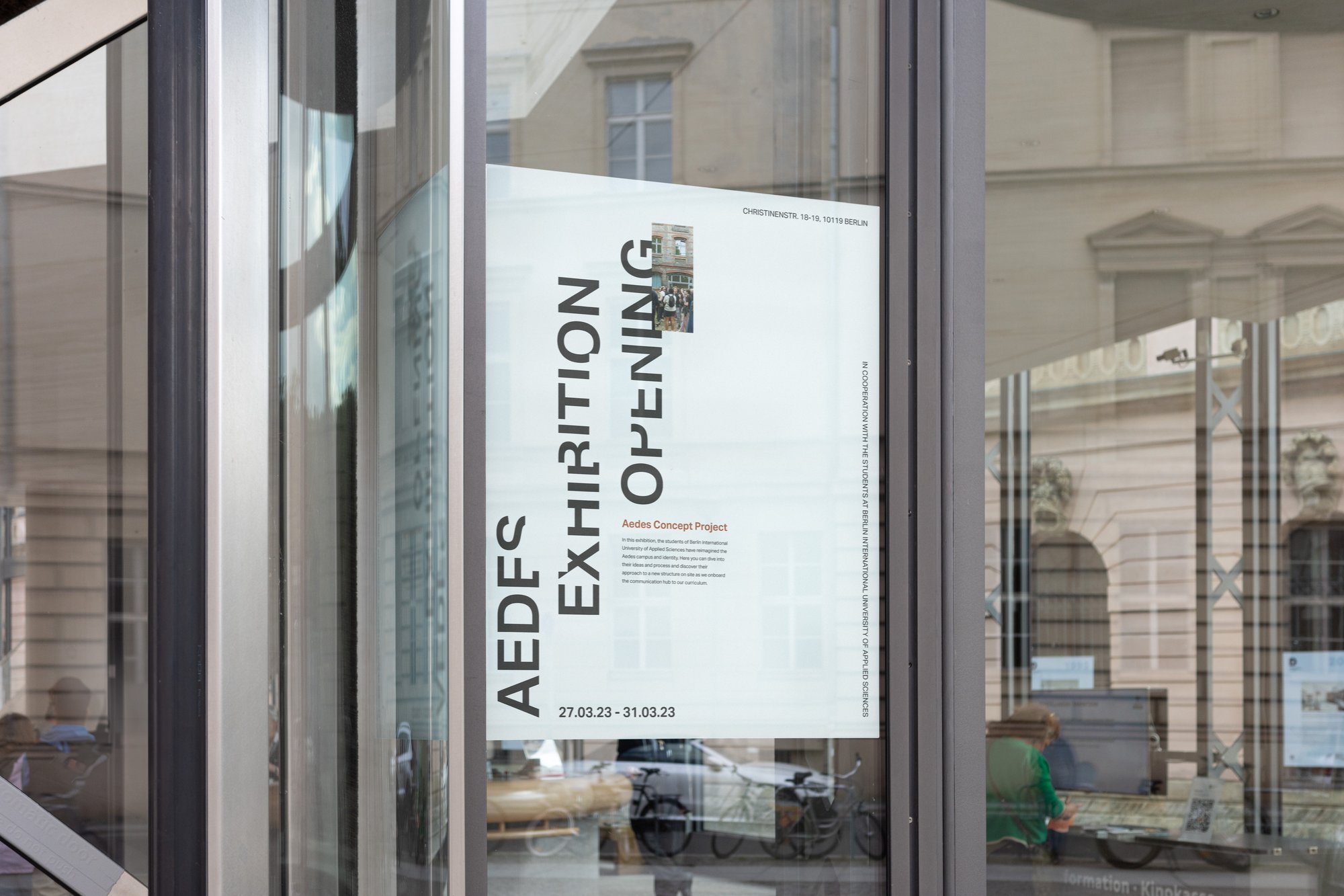Aedes Exhibition Opening poster displayed on a glass entrance door