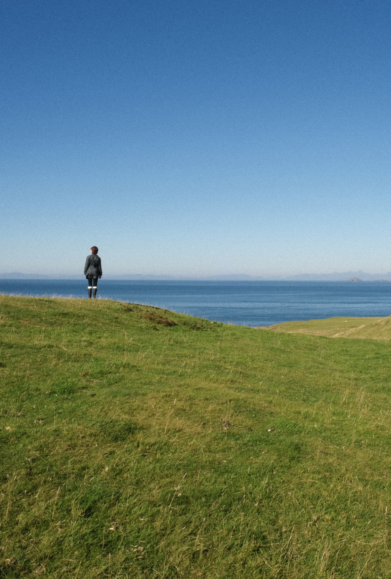 A person standing on a grassy hillside overlooking the sea