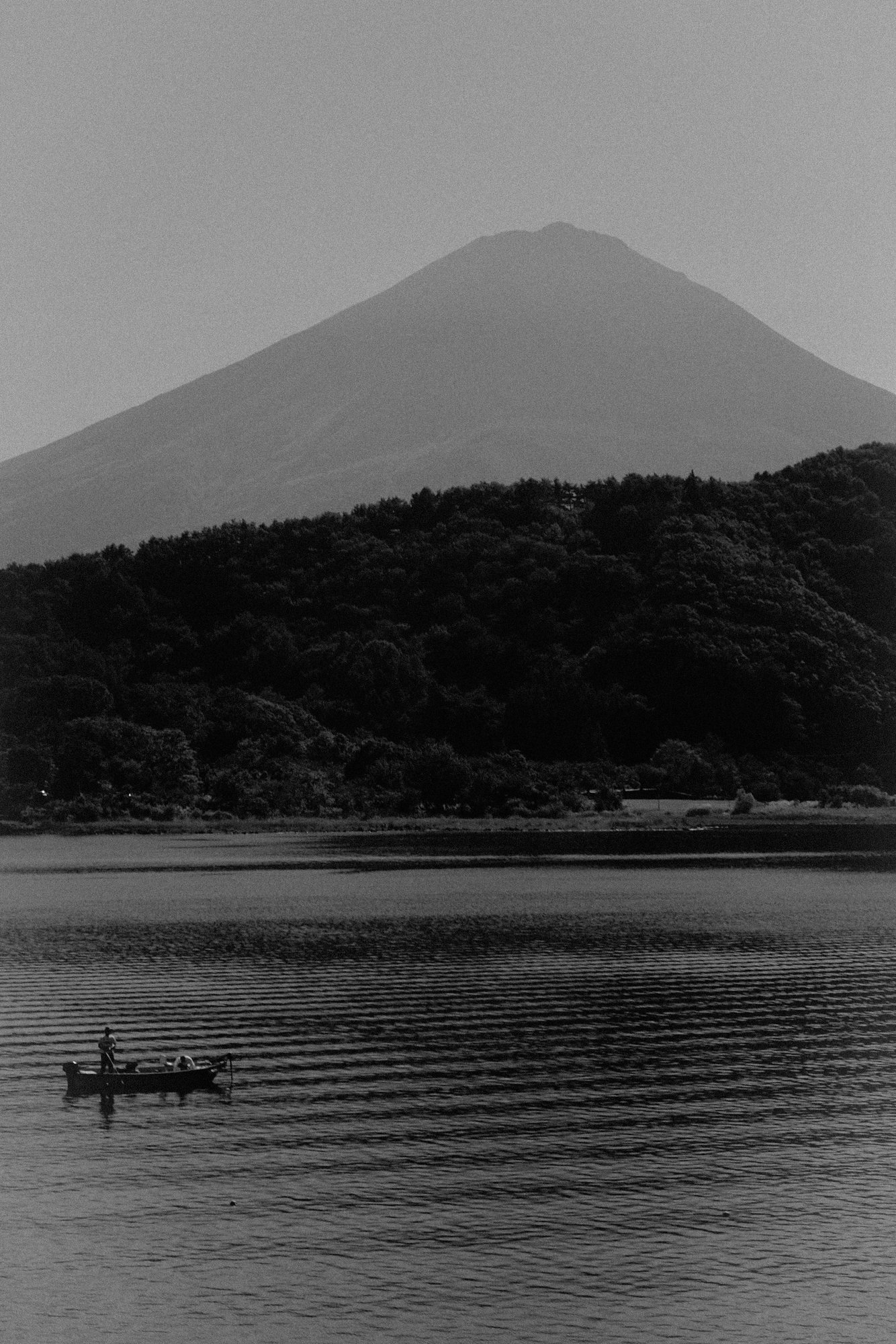 Black and white photograph of Mount Fuji overlooking Lake Kawaguchiko, with a small fishing boat on the water